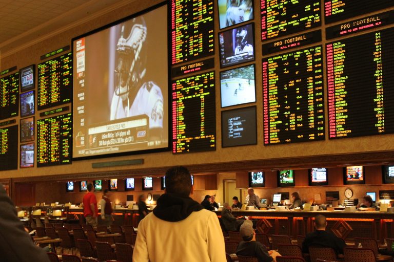 A modern Las Vegas sportsbook with large LED screens, betting counters, and guests watching games.