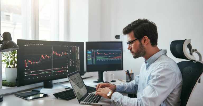 Man focused on computer screens analyzing forex charts while working at a trading desk